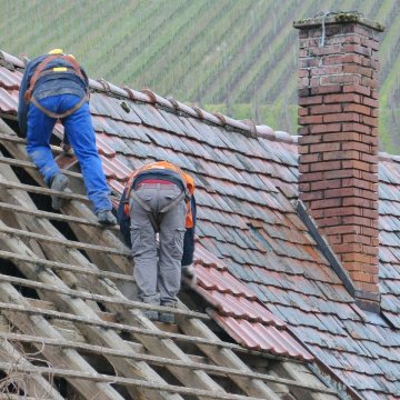 2 people replacing really old tiles on a roof